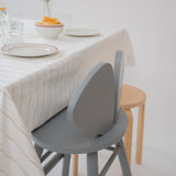 A modern gray wooden dining chair with a curved backrest, shown next to a light wood stool and a table set with a striped tablecloth and plates.
