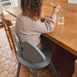 Person sitting at a wooden table eating from a bowl with a spoon, wearing a beige sweater.