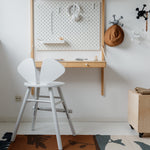 Children's room with a white chair, wooden box, and wall-mounted desk.
