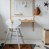 Children's room with a white chair, wooden box, and wall-mounted desk.