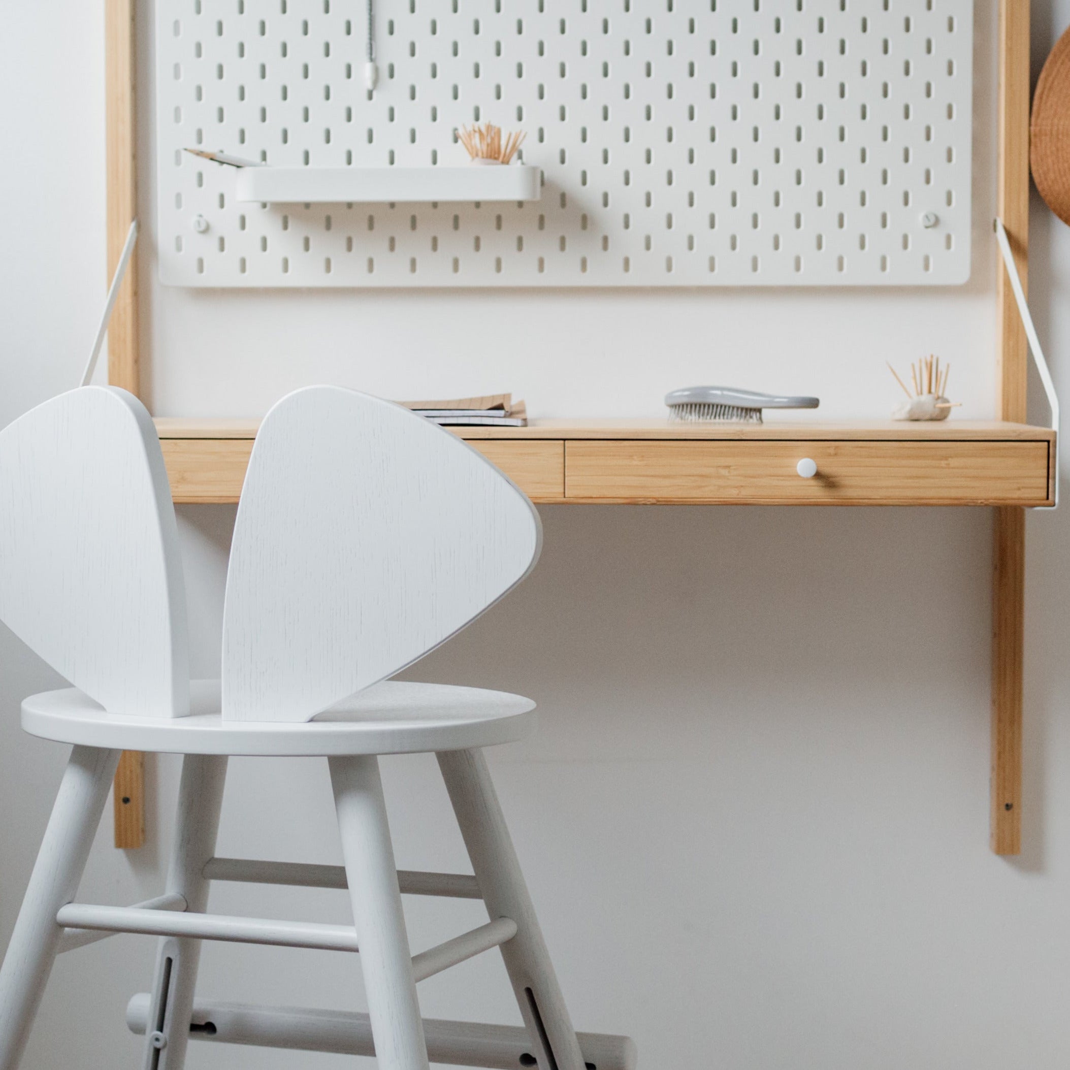 Children's room with a white chair, wooden box, and wall-mounted desk.