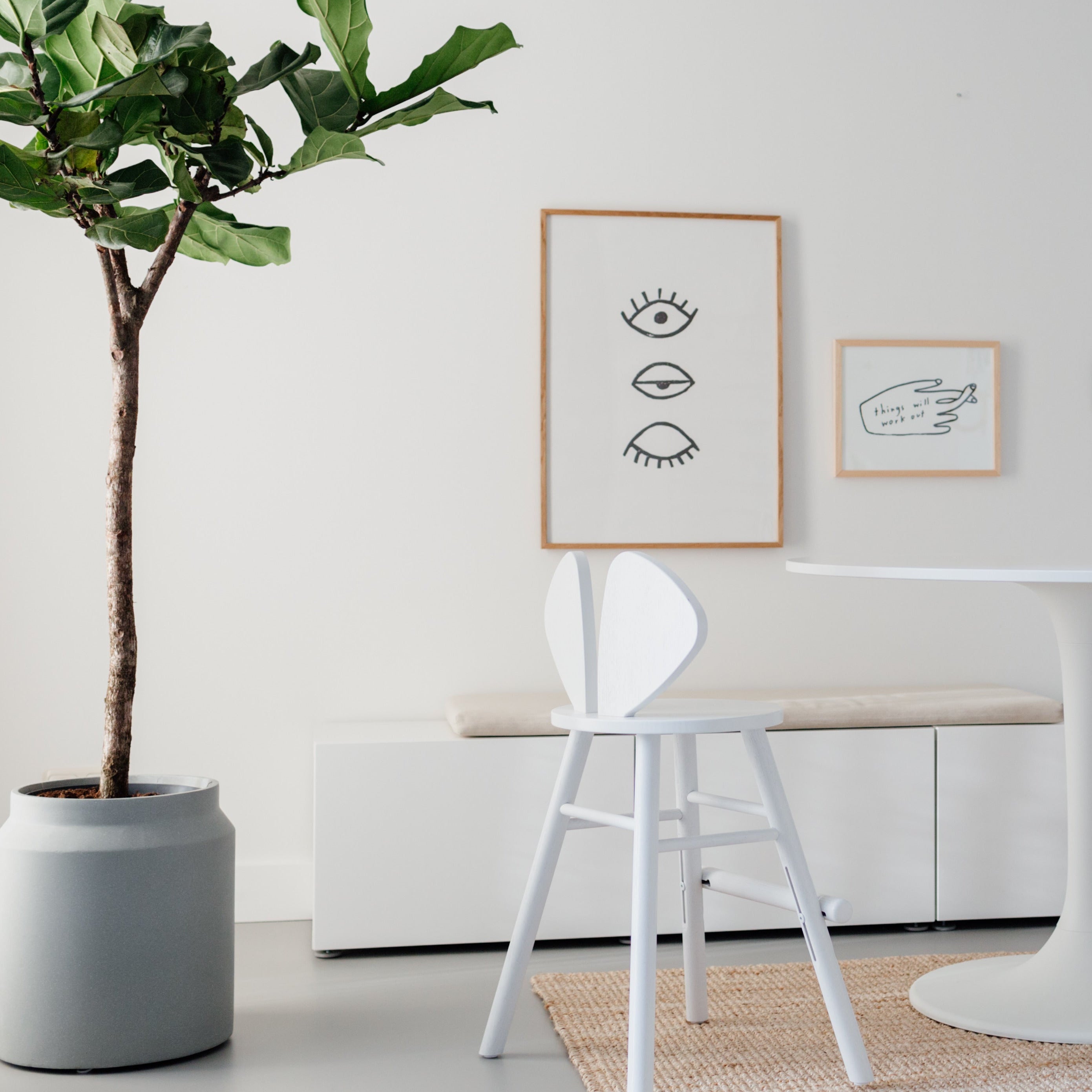Modern dining area with a plant, table, and chairs against a white wall.