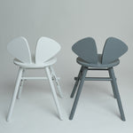 Two modern butterfly-style chairs shown side by side against a light gray studio background. The left chair is white, and the right chair is gray.