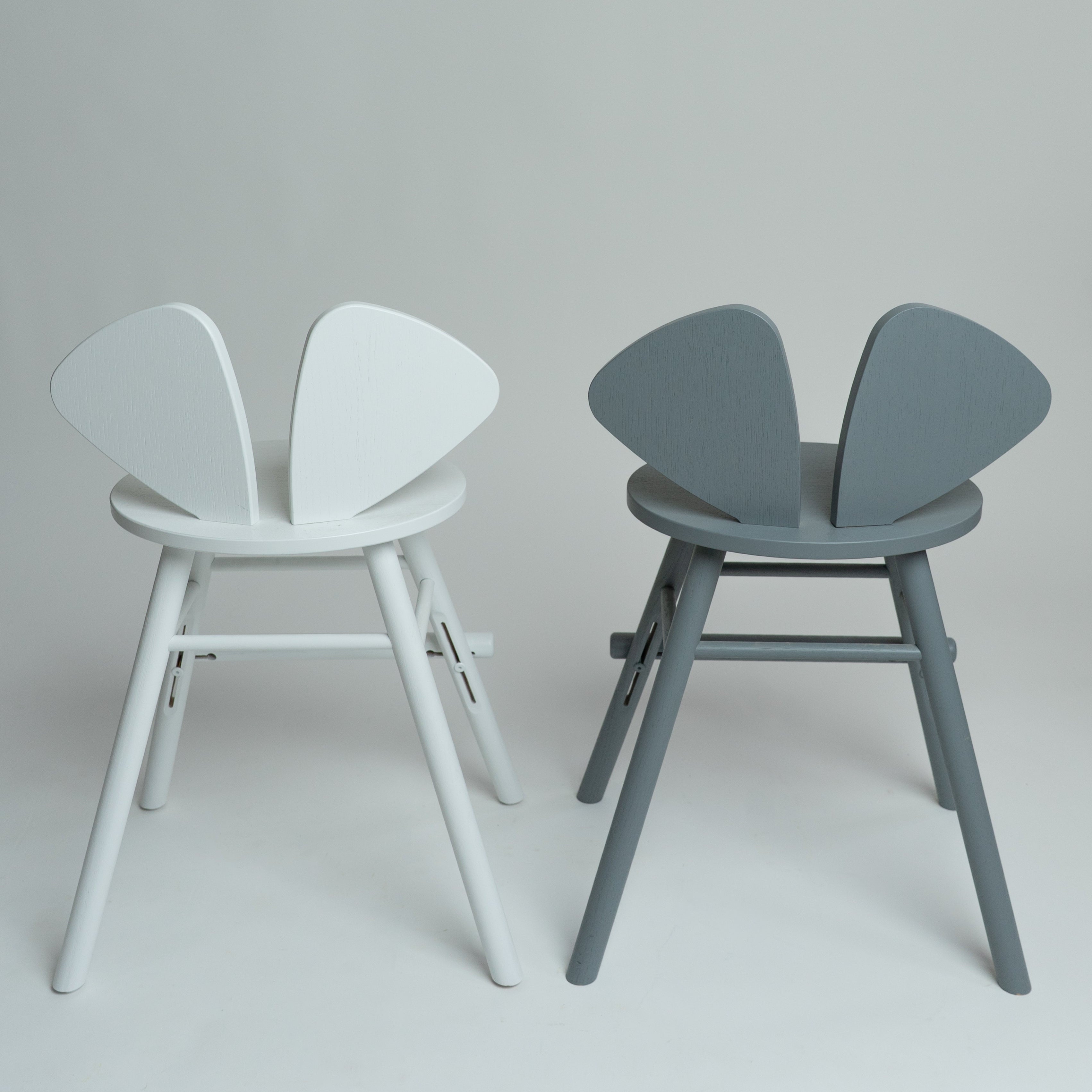 Two modern butterfly-style chairs shown side by side against a light gray studio background. The left chair is white, and the right chair is gray.