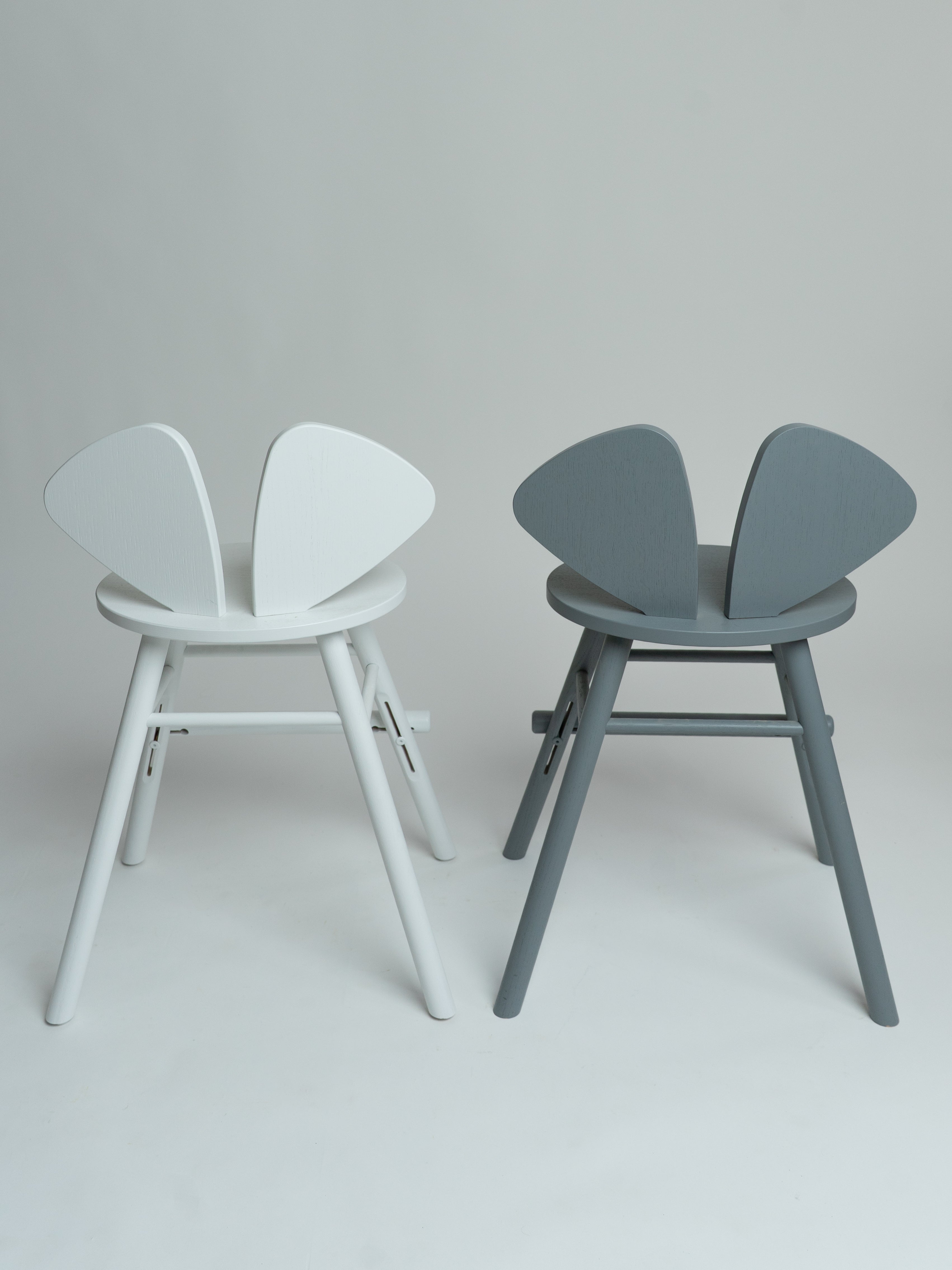 Two modern butterfly-style chairs shown side by side against a light gray studio background. The left chair is white, and the right chair is gray.