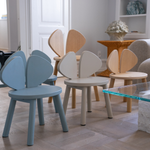 A set of modern wooden children's chairs with curved backrests in light blue, cream, and natural wood finishes, arranged in a bright, contemporary living room.
