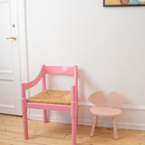 Two pink chairs, one with a woven seat, on a wooden floor.