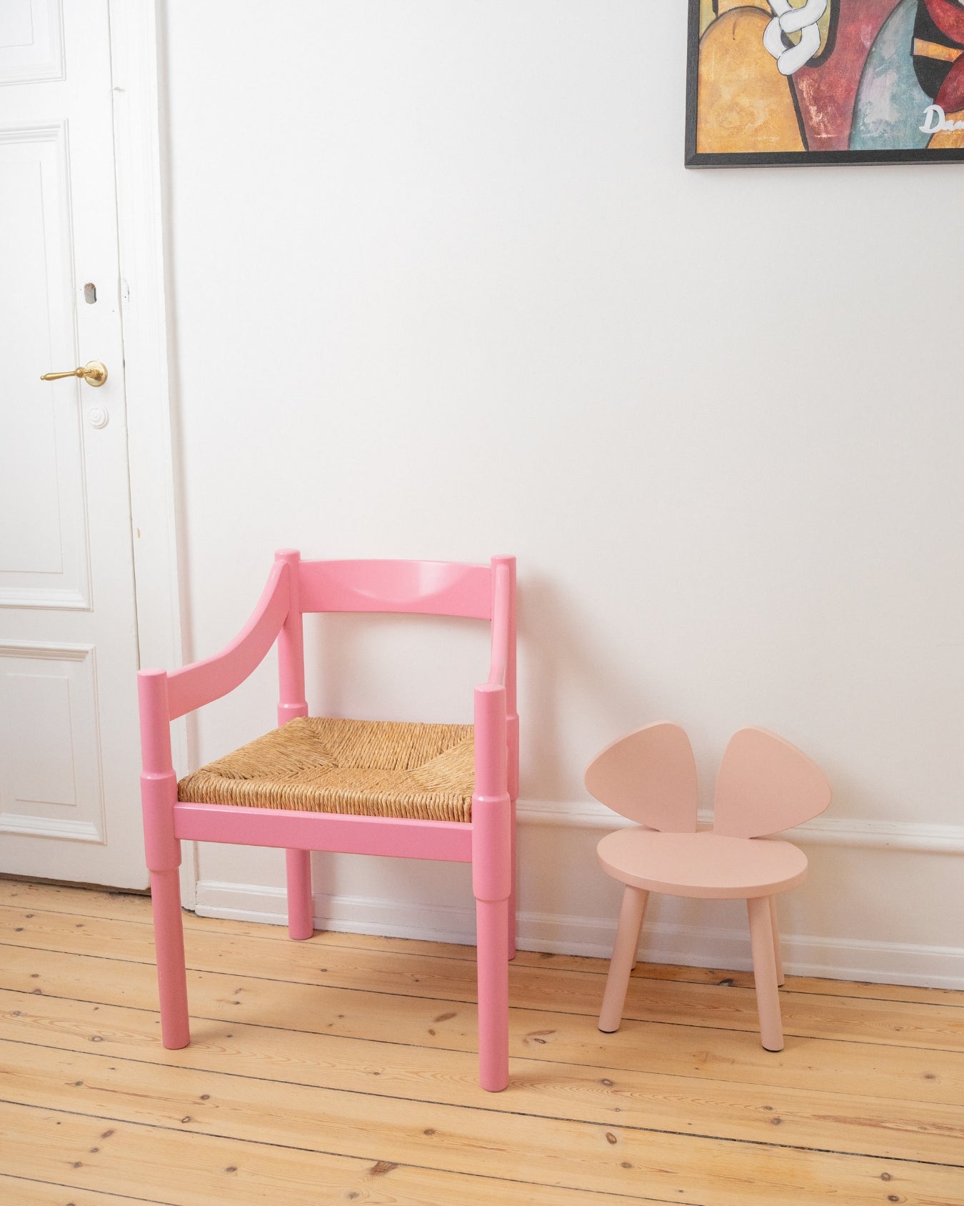 Two pink chairs, one with a woven seat, on a wooden floor.