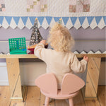 Child playing at a small wooden table with a pink chair, colorful blocks, and a decorative wall.