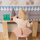 Child playing at a small wooden table with a pink chair, colorful blocks, and a decorative wall.