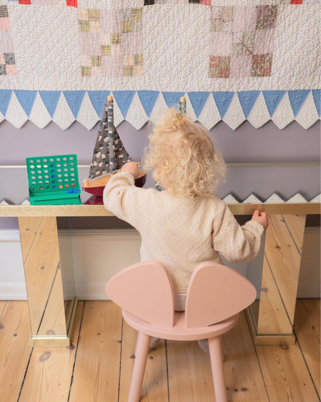 Child playing at a small wooden table with a pink chair, colorful blocks, and a decorative wall.