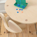 Children's wooden table and chair set with colorful game pieces on a wooden floor.