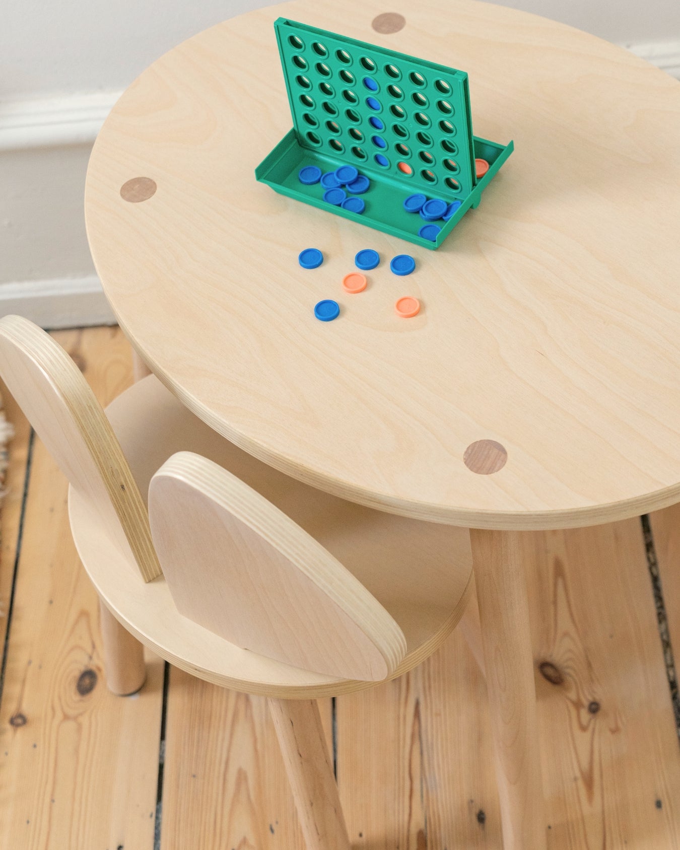 Children's wooden table and chair set with colorful game pieces on a wooden floor.