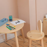Children's wooden table and chair set with art supplies on a wooden floor.
