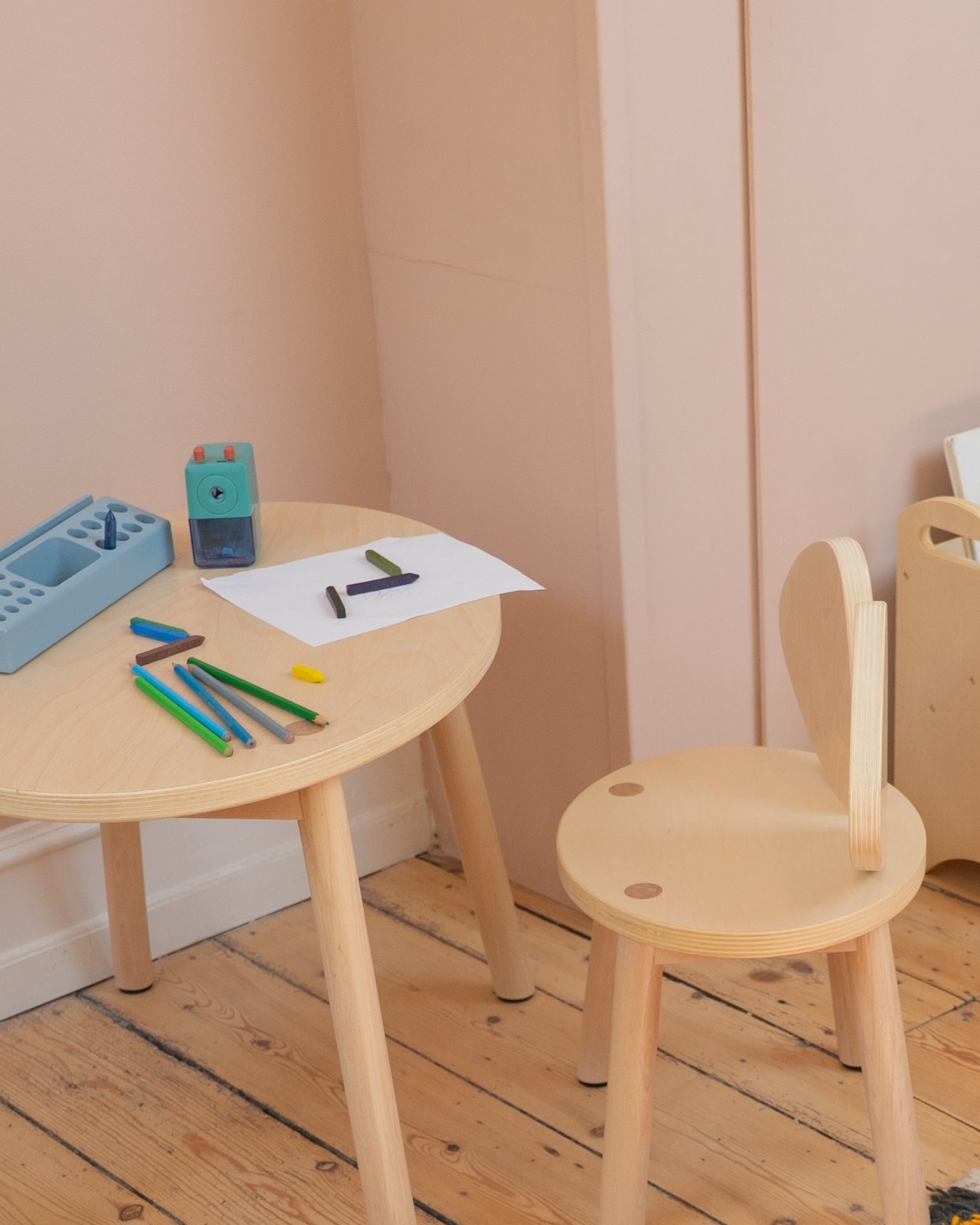 Children's wooden table and chair set with art supplies on a wooden floor.