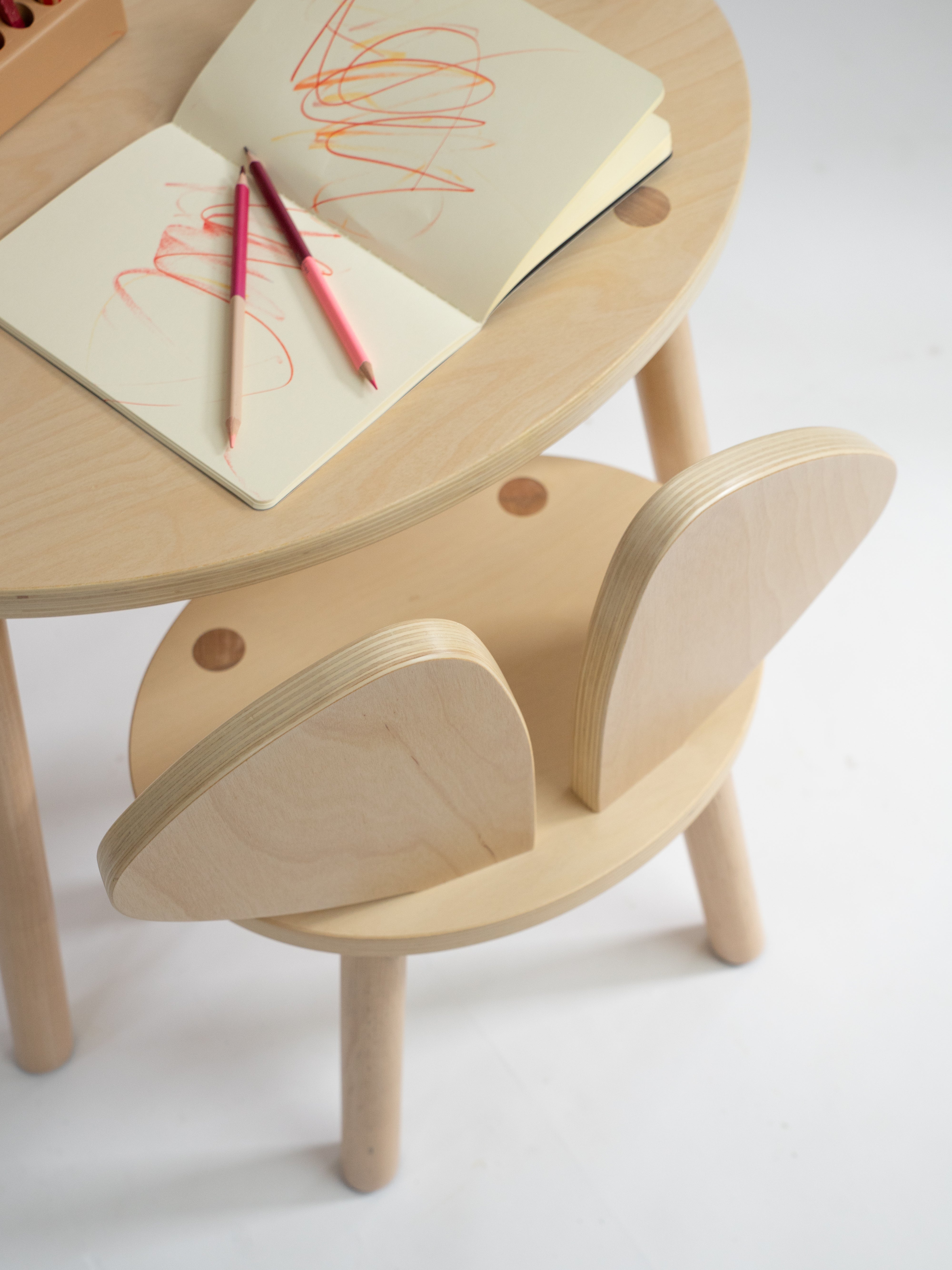 Wooden children's table and chair set with notebooks and pencils on a white background