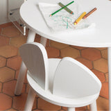 A white wooden chair standing next to a table with kids drawings on it
