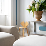 Modern living room with a beige sofa, Mouse Oak Junior chair, and a vase of flowers on a table.