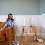 Woman sitting on a brown sofa in a room with wooden flooring and white walls.