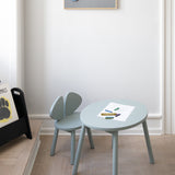 A table and chair set in olive green standing in the middle of the kids room with pencils on it