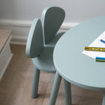 Light blue chair and round table with stationery on a wooden floor.