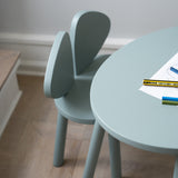 Light blue chair and round table with stationery on a wooden floor.