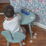 A kid sitting at the table and chair set, playing with cards