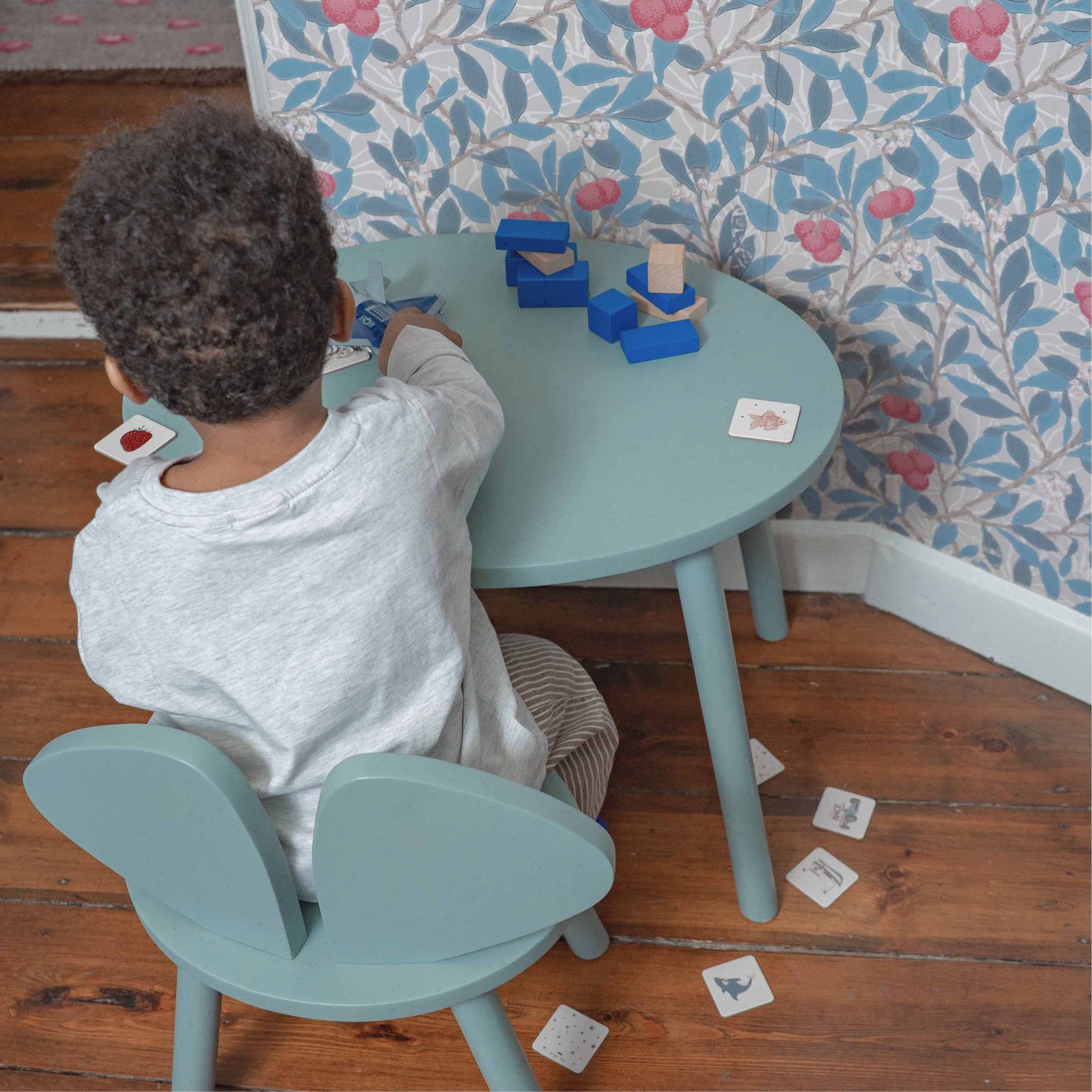 A kid sitting at the table and chair set, playing with cards