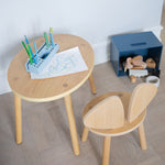 Children's wooden table and chair set with art supplies on a light wood floor.