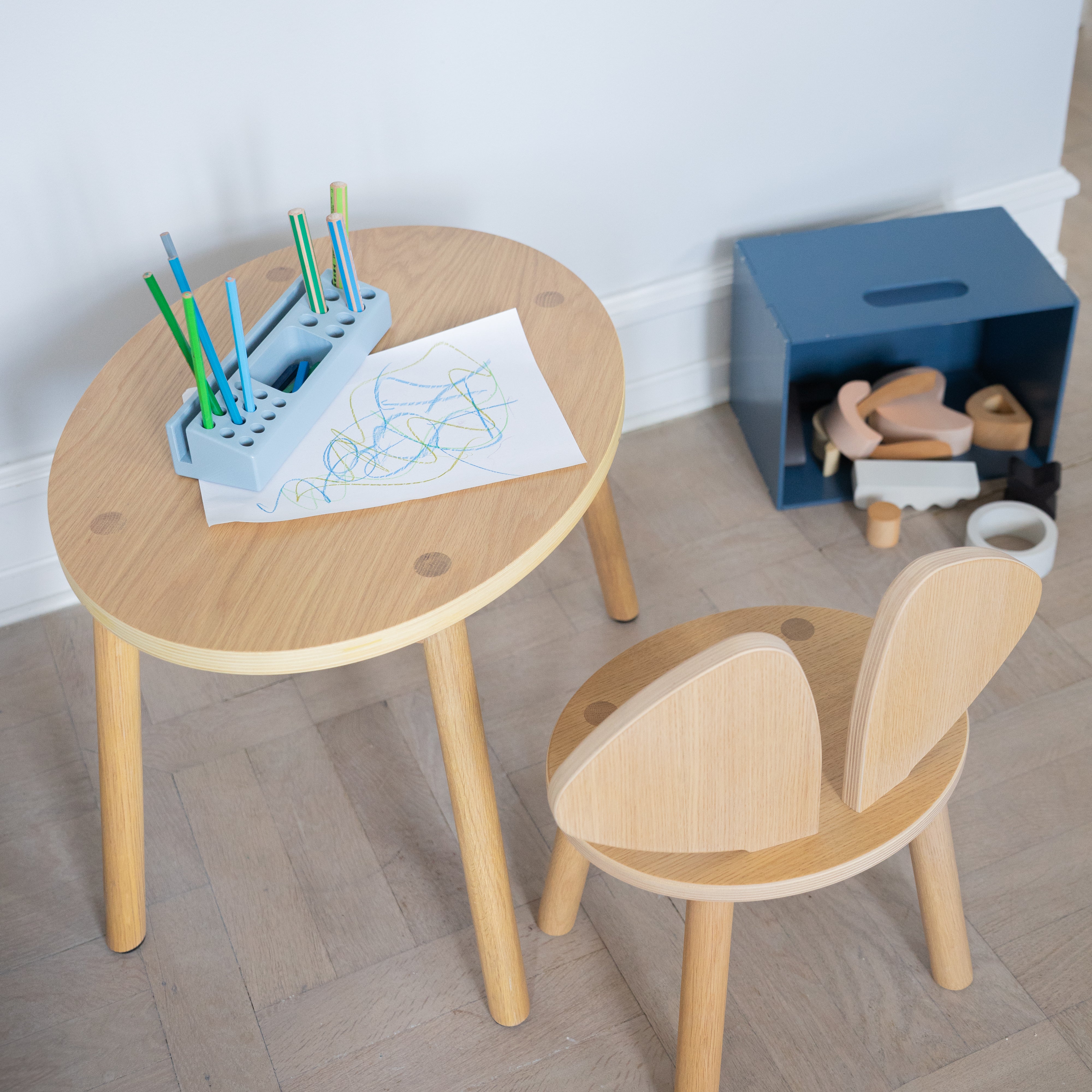 Children's wooden table and chair set with art supplies on a light wood floor.