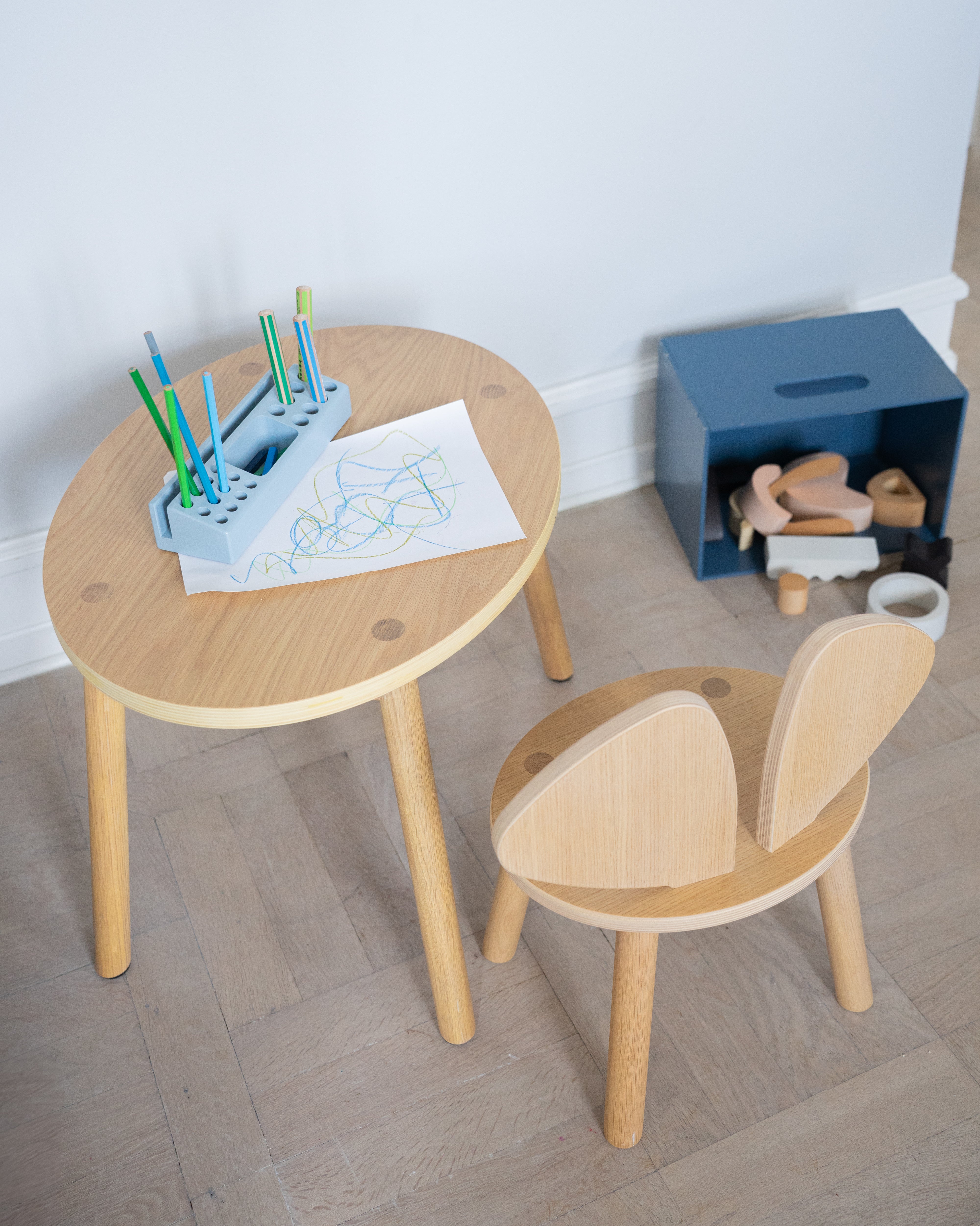 Children's wooden table and chair set with art supplies on a light wood floor.