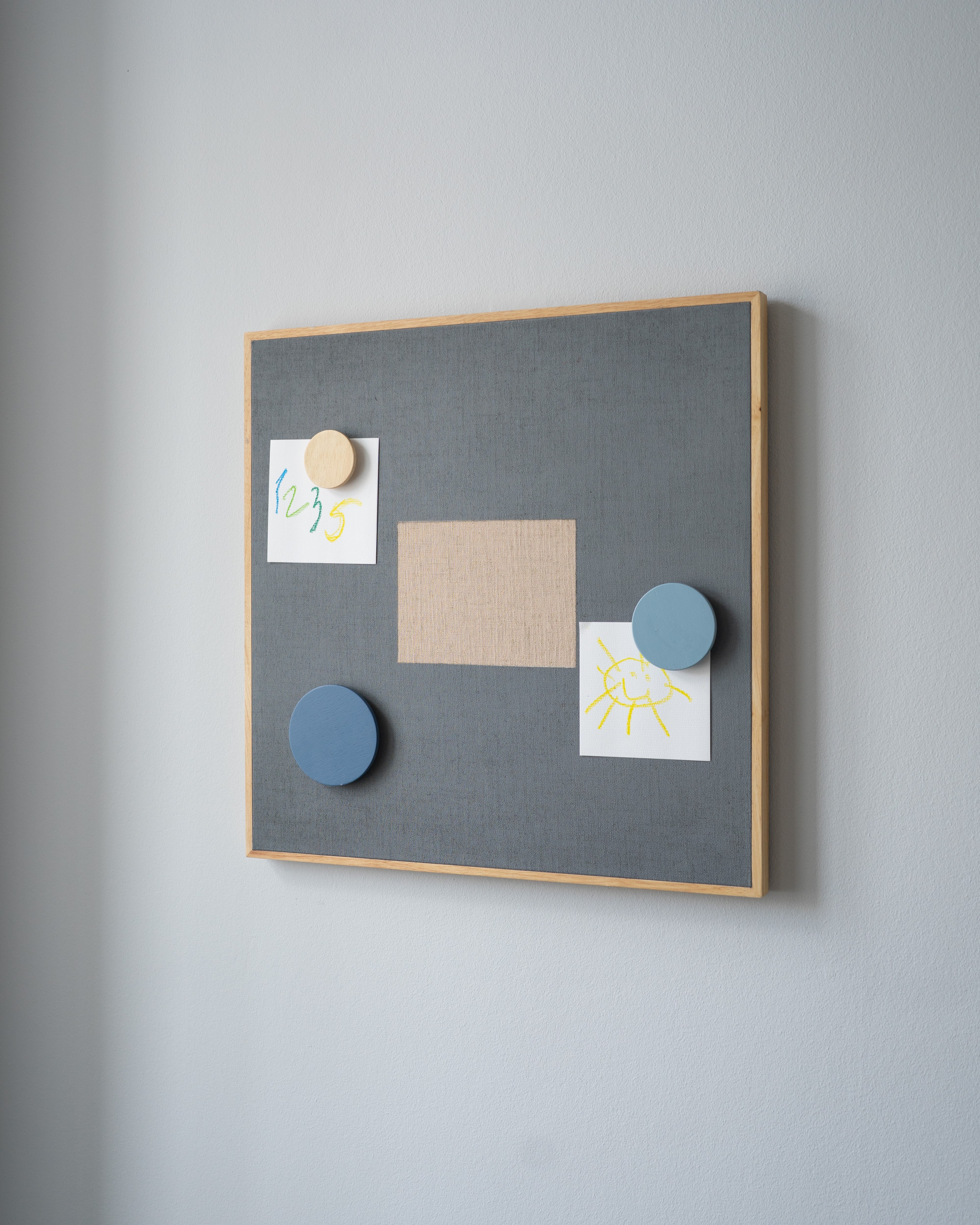 Gray bulletin board with wooden frame on a gray wall, featuring various notes and magnets.