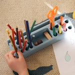 Children's art supplies including colored pencils, scissors, and crayons in a holder on a textured surface.
