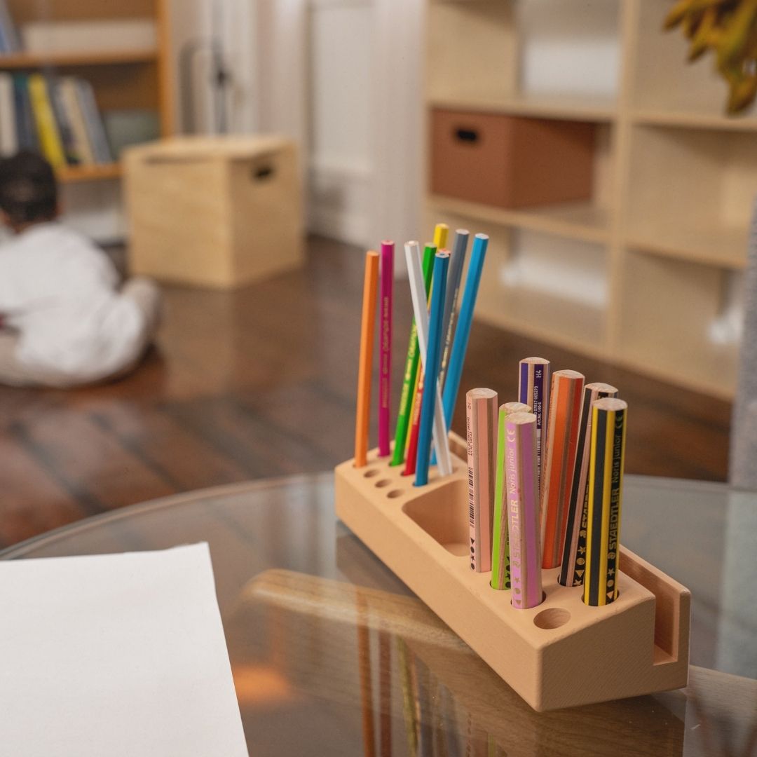 Colorful markers in a wooden holder on a glass table with a blurred indoor background