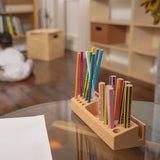 Colorful markers in a wooden holder on a glass table with a blurred indoor background