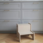 Beige children's chair in a kitchen with gray cabinets and wooden floor.