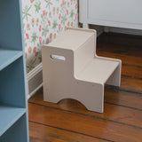 Two-step stool on a wooden floor with a floral-patterned rug and blue furniture in the background.