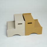 Two minimalist two-step platforms, one in light beige and one in mustard yellow, shown side-by-side on a light gray studio background.