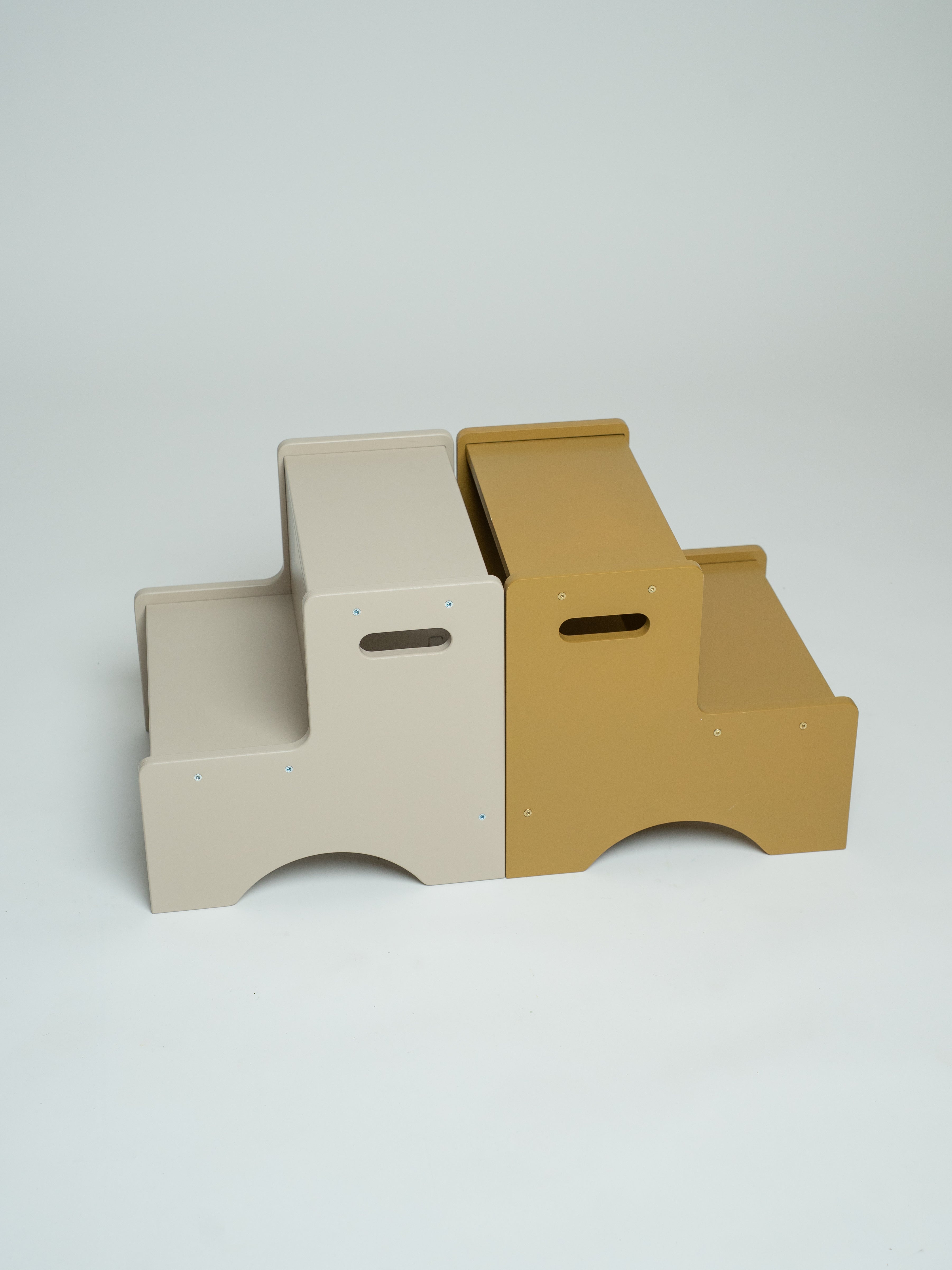 Two minimalist two-step platforms, one in light beige and one in mustard yellow, shown side-by-side on a light gray studio background.