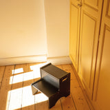 Small black step stool on a wooden floor next to a white wall and yellow cabinet.