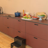 Kitchen with red cabinets, a step stool, and various kitchen items on the counter.
