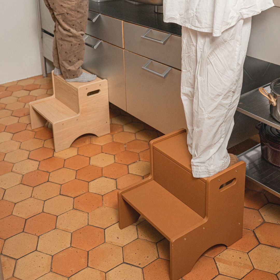 Two step stools being used by people on a hexagonal tiled kitchen floor.