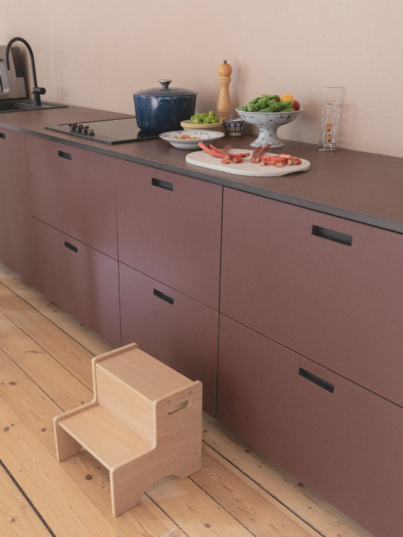 Step stool in a modern kitchen with purple cabinets and a wooden floor.