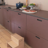 Step stool in a modern kitchen with purple cabinets and a wooden floor.