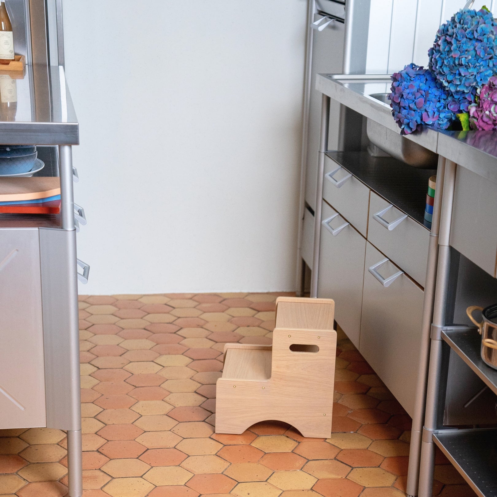 Wooden step stool in a kitchen with tiled floor and cabinets.