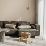 Gray sectional sofa with decorative pillows in a modern living room. Oak Step Up Nofred Chair in front