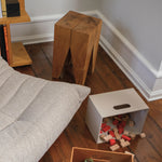 Wooden stools and a white storage box with toys on a wooden floor next to a sofa.