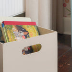 Beige storage box with colorful books on a wooden floor