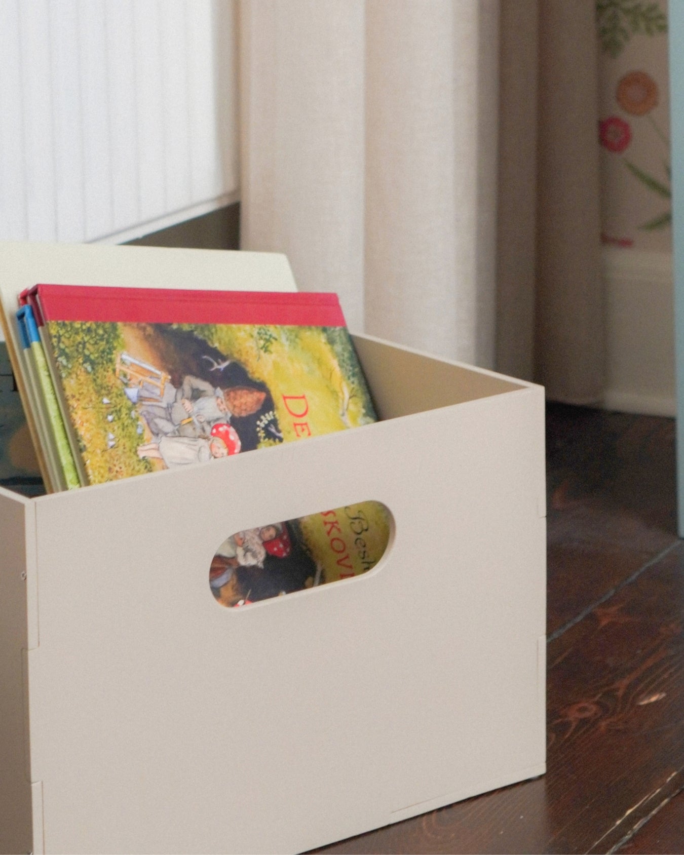 Beige storage box with colorful books on a wooden floor