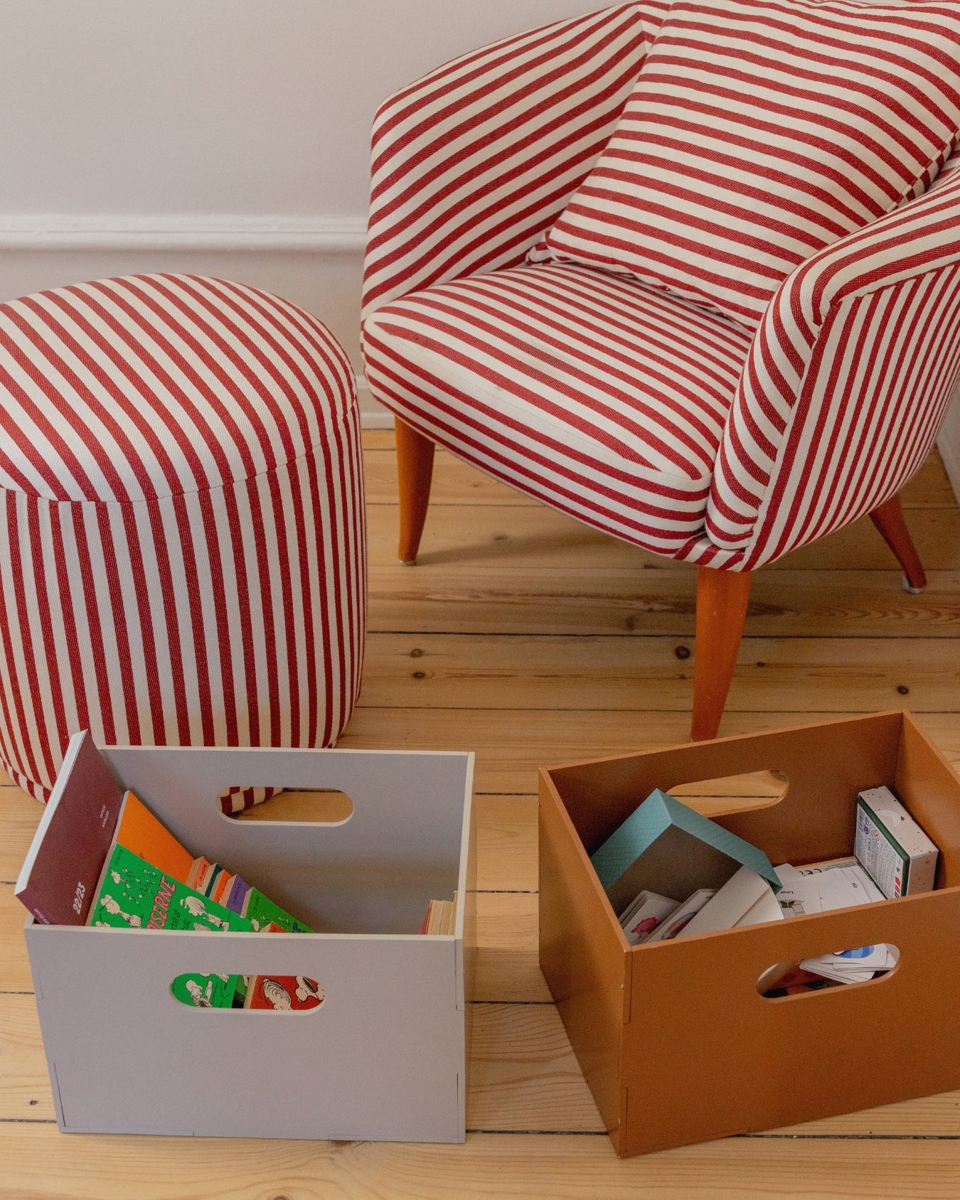 Red and white striped chair and ottoman with storage boxes on a wooden floor.
